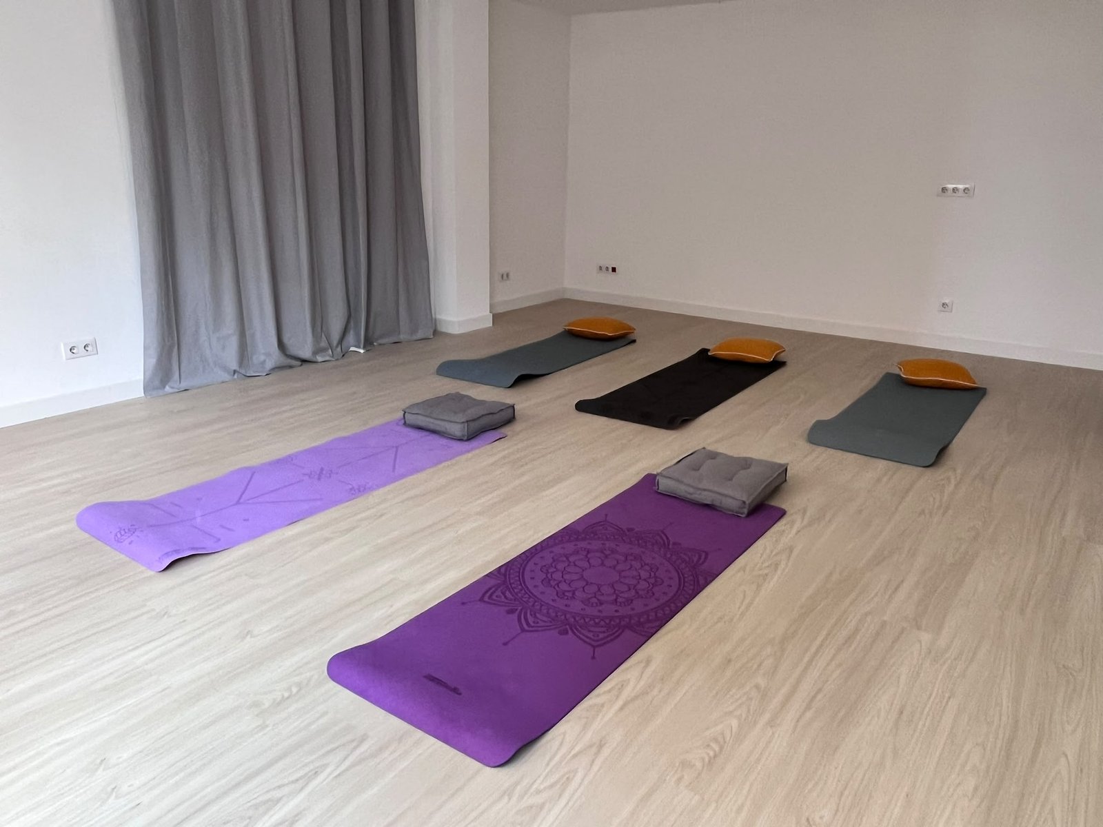 Sala de Cauma a Sant Cugat del Vallès: espai lluminós amb parquet clar, cortines grises, esterilles de ioga i coixins de meditació